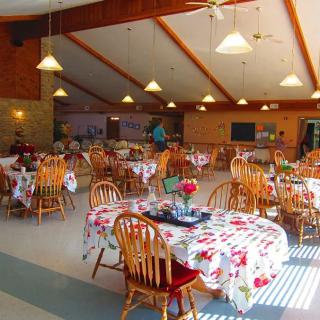 A brightly lit dining hall with decorated tables and wooden chairs, ready for guests.