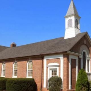 A traditional brick church with a white steeple under a clear blue sky.