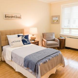A cozy bedroom with a neatly made bed, armchair, and warm lighting.