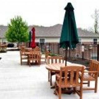 A patio area with wooden tables and chairs, shaded by umbrellas.