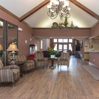 A spacious lobby area with a high ceiling, featuring comfortable seating, a chandelier, and a reception desk.