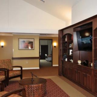 A cozy living room with wooden furniture, a TV on the wall unit, and comfortable seating.