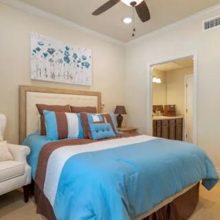 A modern bedroom featuring blue and brown bedding, complemented by a floral artwork and warm lighting.