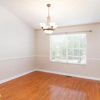An empty dining room with hardwood floors, a chandelier, and a large window letting in natural light.
