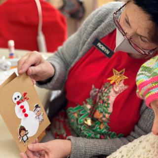 A woman and child engage in holiday crafting, making a snowman card.
