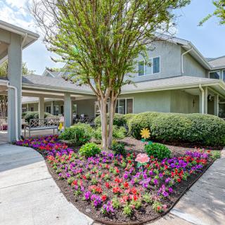 A beautifully landscaped garden with colorful flowers and a tree in front of a house.