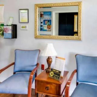 A cozy waiting area with two chairs and a wooden table adorned with a lamp and decorative items, complemented by a large mirror on the wall.