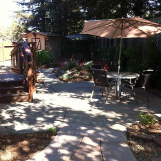 A tranquil backyard patio with outdoor furniture and an umbrella shaded by tall trees.