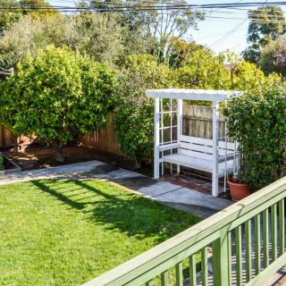 A cozy backyard with a lush green lawn and a white pergola seating area surrounded by tall hedges.