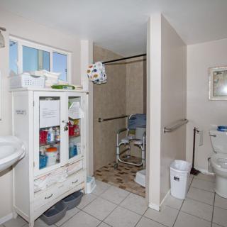 A spacious bathroom equipped with a shower area, toilet, and a storage cabinet. The room features tiled flooring and accessibility aids such as handrails.