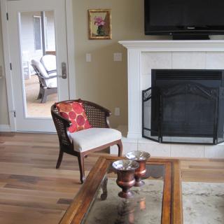 A cozy living room featuring a fireplace, a stylish chair with a red cushion, and a television mounted above the mantel.