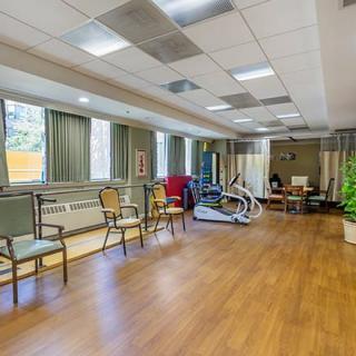 A spacious therapy room with exercise equipment and seating, featuring large windows and bright lighting.