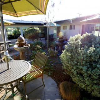 A serene outdoor garden space with a table, chairs, and an umbrella surrounded by lush greenery.