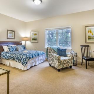 A cozy bedroom with a blue-patterned bedspread, two chairs, and a large window.