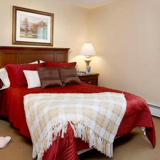 A cozy bedroom with a neatly made bed featuring red bedding, pillows, and a checkered blanket.