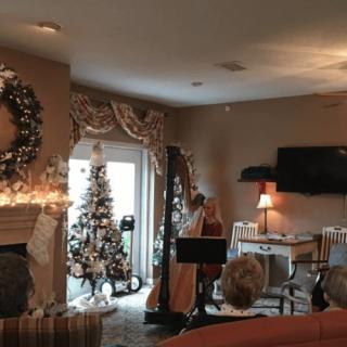 A cozy living room decorated for the holiday season with a Christmas tree and harp.