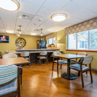 A cozy dining area with wooden flooring, tables, chairs, and a television on the wall.