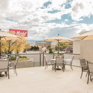 A patio with tables and chairs under umbrellas, set against a city backdrop under a cloudy sky.