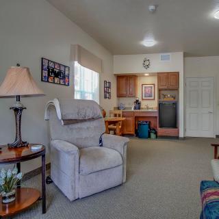 A cozy living room area with a comfortable armchair, side table, and a view of a kitchenette in the background.