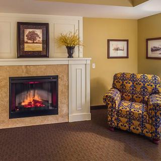 A cozy living room features a fireplace, patterned armchair, and decorative artwork.
