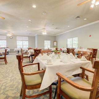 An elegant dining room with neatly set tables and chairs, featuring white tablecloths and warm lighting.
