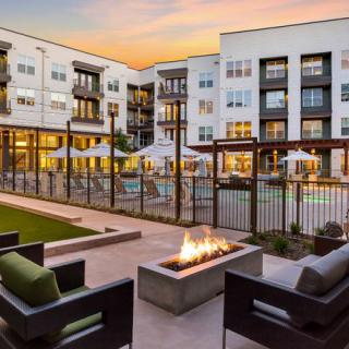 Modern apartment complex featuring an inviting outdoor space with a pool and fire pit at sunset.