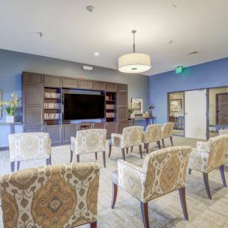 A modern meeting room with patterned chairs arranged facing a large television, surrounded by bookshelves and stylish lighting.