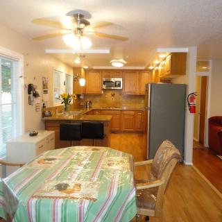 A cozy kitchen with wooden cabinets and a dining area featuring a table and chairs, illuminated by a ceiling fan light.