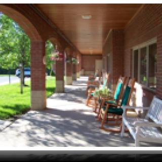 A shaded porch with several rocking chairs and outdoor seating.