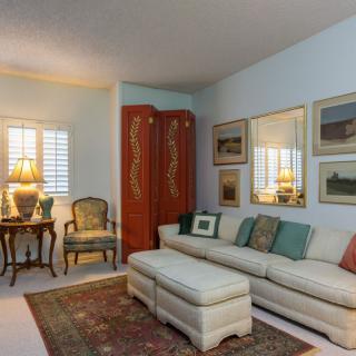 A cozy living room featuring a cream-colored sofa, decorative cushions, framed artwork on the walls, a lamp on a side table, and an ornate screen.
