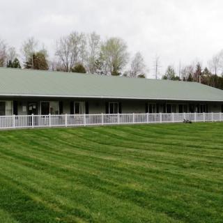 A long building with a green roof and white fence, surrounded by a well-maintained lawn and trees in the background.