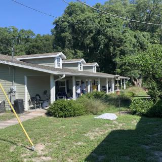 A sunny day at a house with a spacious front yard and surrounding trees.