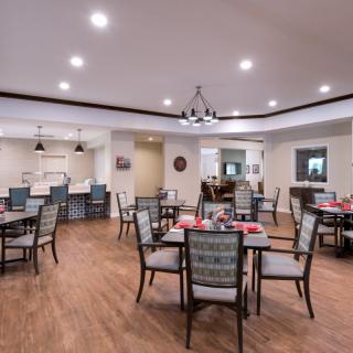 A modern dining area with neatly arranged tables and chairs, featuring elegant lighting and a wooden floor.