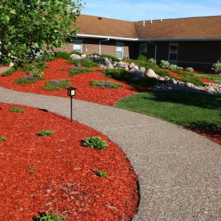 A well-maintained garden with red mulch and a winding concrete pathway leading to a building.