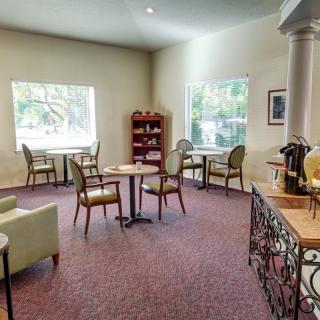 A cozy cafe interior with tables and chairs, featuring a bookshelf and large windows.
