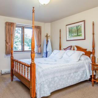 A cozy bedroom featuring a wooden four-poster bed with white bedding, a window with curtains, and carpeted flooring.