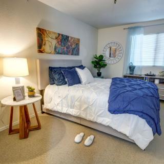 A cozy bedroom with a neatly made bed, bedside lamp, and slippers on the floor.