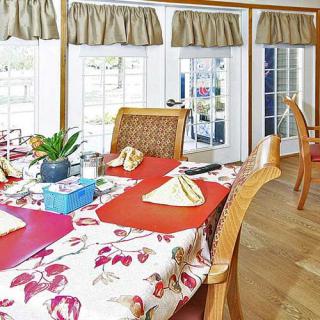 A bright dining room with a floral tablecloth, neatly arranged place settings, and large windows letting in natural light.