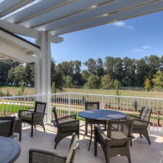 Outdoor patio area with tables and chairs under a pergola, surrounded by nature.