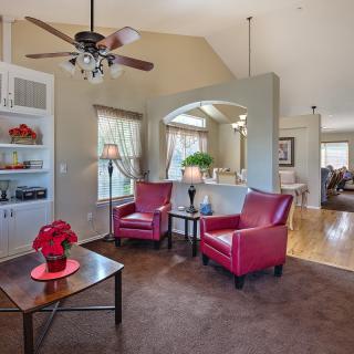 A cozy living room featuring two red chairs, a wooden coffee table, and a ceiling fan, with ample natural light flooding through the windows.