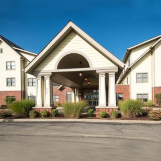 A large building with an entrance featuring columns and surrounding landscaping under a clear blue sky.