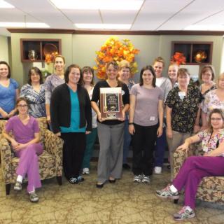 A team poses together in an office setting, holding an award.