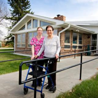 A caregiver and an elderly person with a walker standing outside a nursing home.