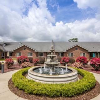 A serene courtyard featuring a beautiful fountain surrounded by vibrant flowers and well-maintained greenery.