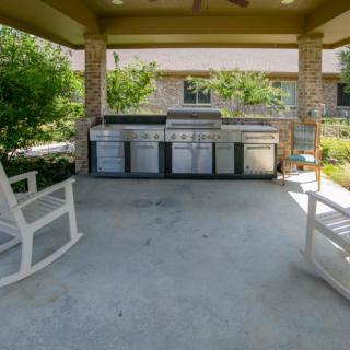A cozy outdoor patio with rocking chairs and a grill under a covered area.