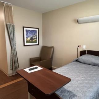 A clean and simple hospital room with a single bed, chair, and artwork on the wall.