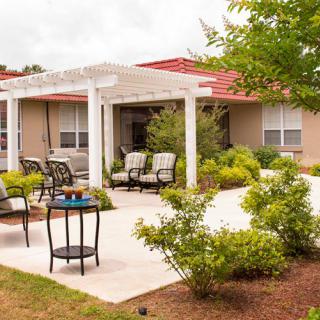 A cozy patio with outdoor seating under a pergola surrounded by lush garden landscaping.