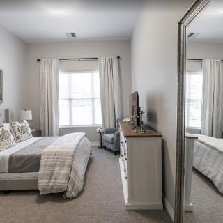 A cozy bedroom with neutral tones, featuring a bed, dresser, and large mirror.