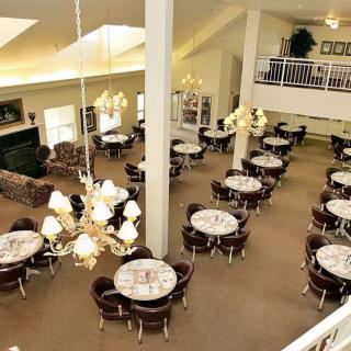A spacious dining area with multiple round tables set with white tablecloths, elegant chandeliers, and a carpeted floor.