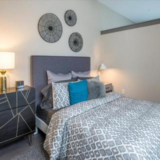A modern bedroom featuring a stylish bed with patterned bedding, decorative pillows, and wall art.